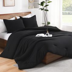 a bed with black sheets and pillows in a white room next to a potted plant