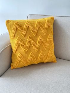 a yellow knitted pillow sitting on top of a gray couch next to a white chair