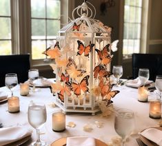 a white table topped with a lantern filled with lots of orange butterflies on top of it