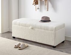 a white bench with a hat on it next to a pair of slippers and coat rack