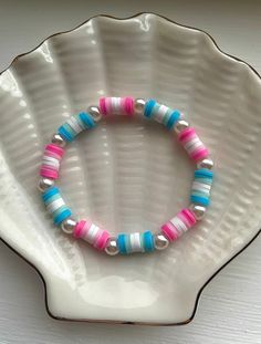 a pink, blue and white beaded bracelet sits on a seashell shell plate