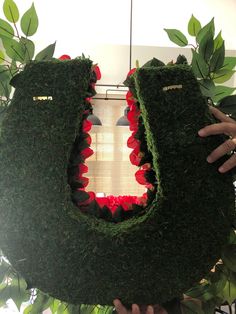 someone is holding up a fake dinosaur head made out of grass and red flowers in front of a window