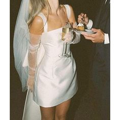 a woman in a short white dress holding a plate with food on it and a man in a suit standing next to her