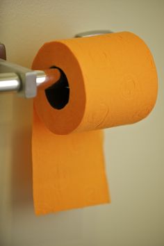 an orange roll of toilet paper is hanging on the wall next to a metal bar