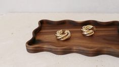 two gold earrings sitting on top of a wooden tray