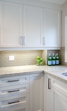 a kitchen with white cabinets and marble counter tops, along with green vases on the sink