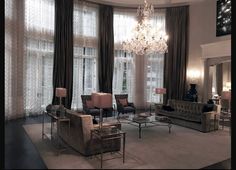 a living room with couches, chairs and chandelier in front of large windows