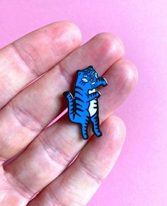 a small blue tiger brooch sitting on top of a pink surface in someone's hand