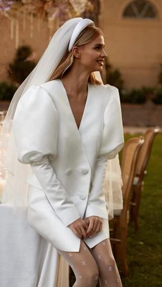 a woman wearing a white dress and veil standing in front of a table with candles