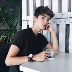 a young man sitting at a table with a cup of coffee