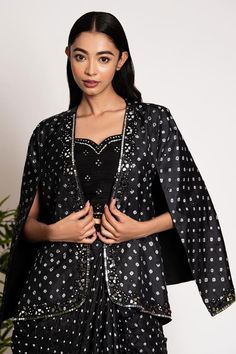 Black silk blazer with all over bandhani patterns highlighted by mirrorwork embellishments. Comes with matching drape skirt and a padded bralette.
Components: 3
Pattern: Embroidered
Type Of Work: Bandhani, Mirrorwork
Neckline: Blazer: Open, Bralette: Sweetheart
Sleeve Type: Blazer: Cape Sleeves, Bralette: Sleeveless
Fabric: Silk
Color: Black
Other Details: 
Attached lining
Length:
Blazer: 24 inches
Drape Skirt: 42 inches
Bralette: 14 inches
Disclaimer: These are made to order designer styles, he Festive Party Outerwear With Dupatta, Elegant Traditional Drape Outerwear For Party, Elegant Party Outerwear With Traditional Drape, Designer Festive Outerwear For Party, Designer Festive Party Outerwear, Formal Festive Cape Set, Traditional Silk Outerwear For Party, Traditional Silk Party Outerwear, Designer Black Festive Outerwear