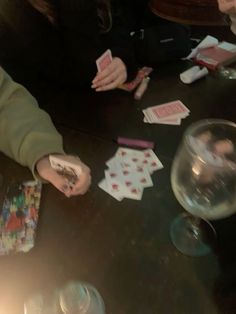 two people playing cards at a table with wine glasses and other items on the table