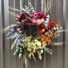 a floral wreath hanging on the side of a metal door with grass and flowers in it