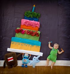 a baby girl standing in front of a cake made to look like it's falling off