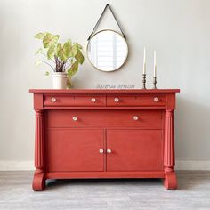 a red dresser with two candles and a potted plant on top, against a white wall