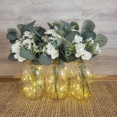 three vases filled with white flowers and greenery