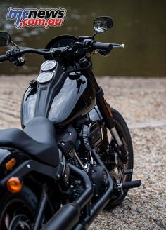 a black motorcycle parked on top of a gravel covered ground next to a body of water