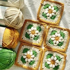 four crocheted squares with white flowers and green leaves on them next to balls of yarn