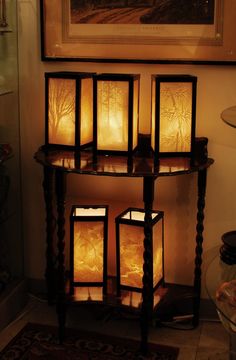 four lit candles sitting on top of a wooden stand in front of a painting and rug