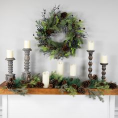 a mantle with candles, pine cones and greenery