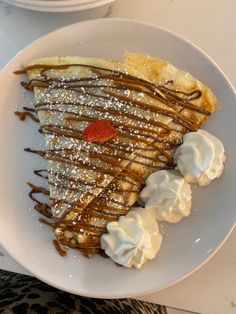 a white plate topped with french toast covered in whipped cream and chocolate sauce next to a bowl of strawberries