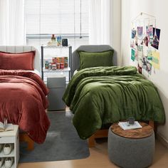 two beds in a bedroom with red and green comforters on the covers, one bed has a gray footstool next to it