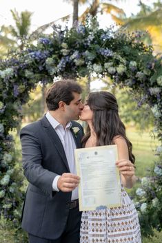 a bride and groom kissing in front of a floral arch with an open letter on it