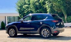 a blue mazda cx - 5 parked in front of a building with trees behind it