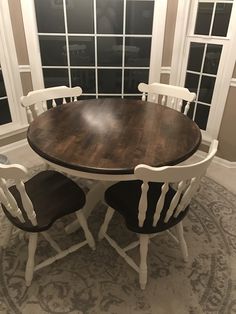 a dining room table with four chairs in front of a window and an area rug on the floor