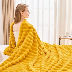 a woman wrapped in a yellow blanket on top of a bed