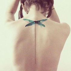 the back of a woman's body with a green dragonfly tattoo on it