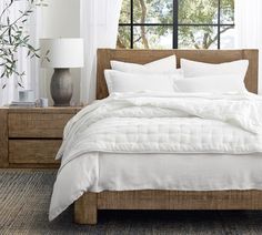 a bed with white linens and pillows in front of a window, next to a lamp