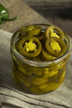 pickled jalapenos in a glass jar on a cloth with a wooden spoon