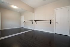 an empty room with mirrors and rails in the wall, along with black hardwood flooring