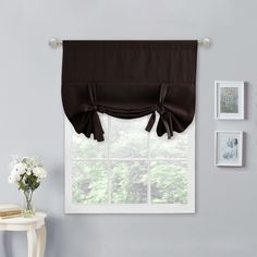 a living room with a window covered in black curtains and white flowers on the table