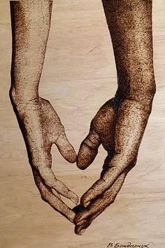 two hands holding each other in the shape of a heart on top of a piece of wood