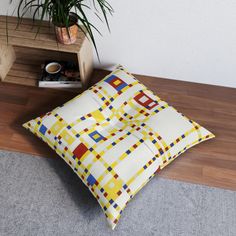 a square pillow on the floor next to a potted plant and coffee mugs