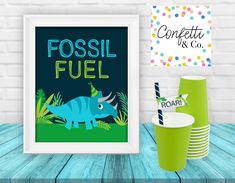 a table topped with green cups and plates next to a framed poster that says fossil fuel