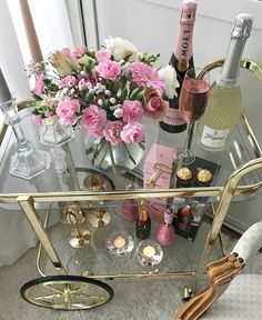 a gold bar cart with pink flowers and champagne bottles on the top is sitting in front of a window