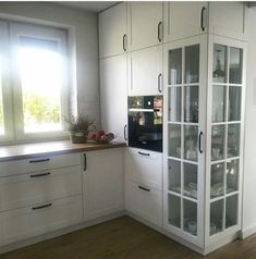 a kitchen with white cabinets and wood flooring in front of a window that is open to the outside