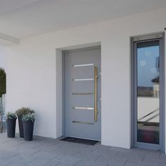 two planters with plants in front of a white wall and door on the sidewalk