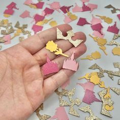 a hand is holding several pieces of paper with glitter on them and gold, pink, and yellow shapes