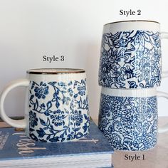 two blue and white coffee mugs sitting next to each other on top of books