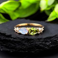 an opal and peridolite ring on top of a rock with leaves in the background