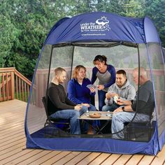 a group of people sitting around a table in a blue tent on top of a wooden deck