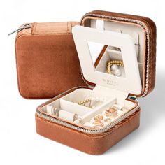 an open brown case with jewelry inside on a white surface and two rings in it