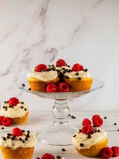 small cupcakes with cream and raspberries on a glass cake platter