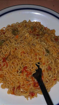 a white plate topped with noodles and vegetables next to a black fork on top of a table