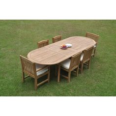 a wooden table with six chairs and a bowl of fruit on it in the grass