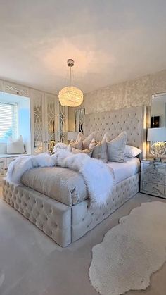 a large white bed sitting inside of a bedroom next to a mirror table and lamp